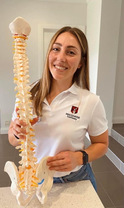 Tayla McDonald, Chiropractor. She is smiling and holding a model of the spine.